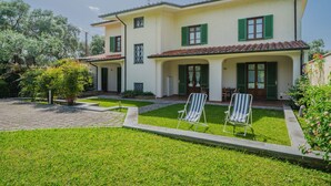 Una casa a due piani con un portico coperto e un piccolo giardino.