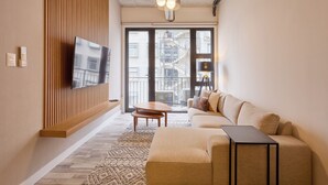 Ett modernt vardagsrum med en stor platt-TV som är monterad på en väggpanel av trä, en beige soffa, ett litet soffbord i trä och en mönstrad matta.