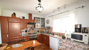 A kitchen with wooden cabinets, a white dishwasher, a microwave, and a dining table with chairs. - Villa 'Casa Papa' with Private Pool, Private Terrace and Wi-Fi (San Fulgencio)