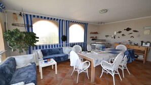 A dining area with a table, chairs, and a sofa. There is a plant, a ceiling fan, and a kitchen area in the background. - Villa 'Casa Papa' with Private Pool, Private Terrace and Wi-Fi (San Fulgencio)
