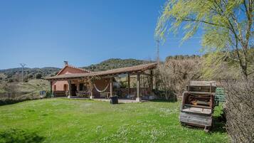 A rustic house with a tiled roof, a covered patio, and a grassy yard.