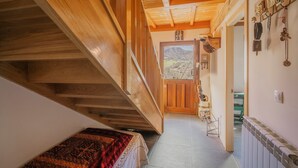 Un couloir étroit, avec un escalier en bois d’un côté, un lit recouvert d’une couverture à motifs et une vue sur l’extérieur par une porte.