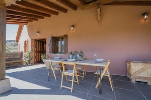Un patio al aire libre con una mesa de madera dispuesta para comer, rodeada de sillas y un rústico caja de madera a un lado.