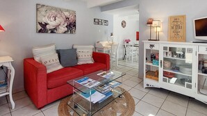 A living room with a red sofa, a glass coffee table, a white cabinet, and a painting on the wall. - Beautiful home in Plérin with WiFi (Plérin)