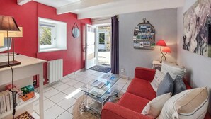 A living room with a red sofa, a glass coffee table, and a red lamp. There is a bookshelf with books and a chessboard. A door leads to an outdoor area with a view. - Beautiful home in Plérin with WiFi (Plérin)