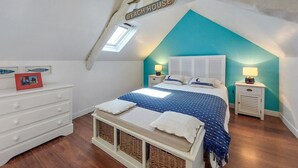A bedroom with a sloped ceiling, a bed with a blue and white striped bedspread, two bedside tables with lamps, a white dresser, and a small framed picture on the dresser. - Beautiful home in Plérin with WiFi (Plérin)