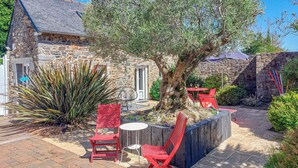 An outdoor seating area with stone walls, red chairs, and a large tree. - Beautiful home in Plérin with WiFi (Plérin)