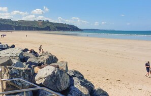 Uma praia com grandes rochas em primeiro plano, céu claro e uma vista distante da costa.