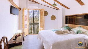Une chambre à coucher comprenant un lit, un bureau, une chaise, une télévision et un balcon avec vue sur les arbres.