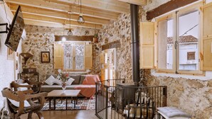 Un intérieur rustique avec un mur en pierre, des meubles en bois, une cheminée et une vue sur l’extérieur.