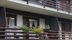 Un immeuble à plusieurs étages doté de balcons, de plantes en pot et d’un espace extérieur aménagé avec des sièges.