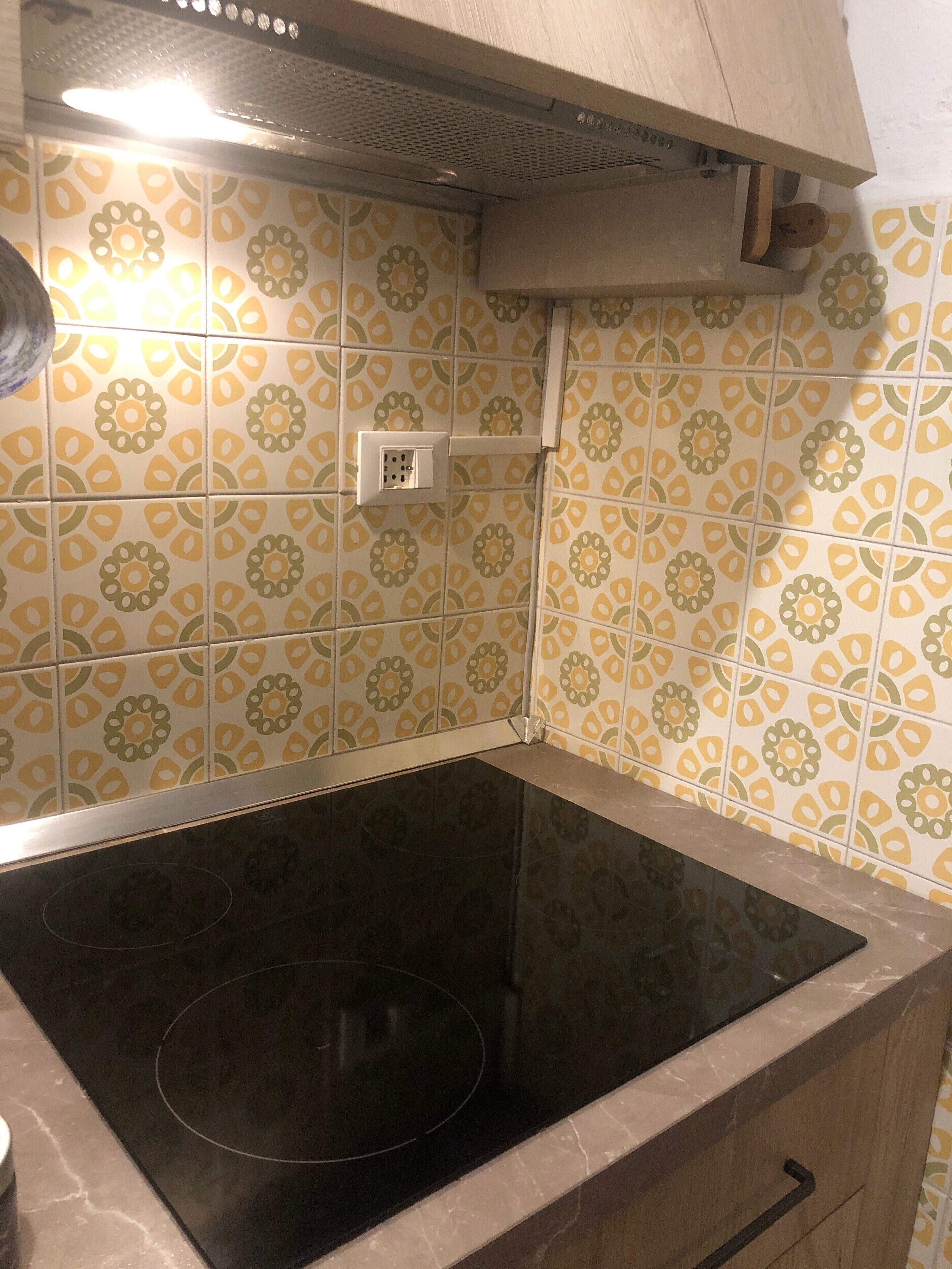 A kitchen with a black induction cooktop, a vent hood, and patterned yellow and green tiles.