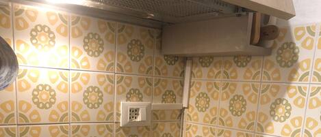 A kitchen with a black induction cooktop, a vent hood, and patterned yellow and green tiles.