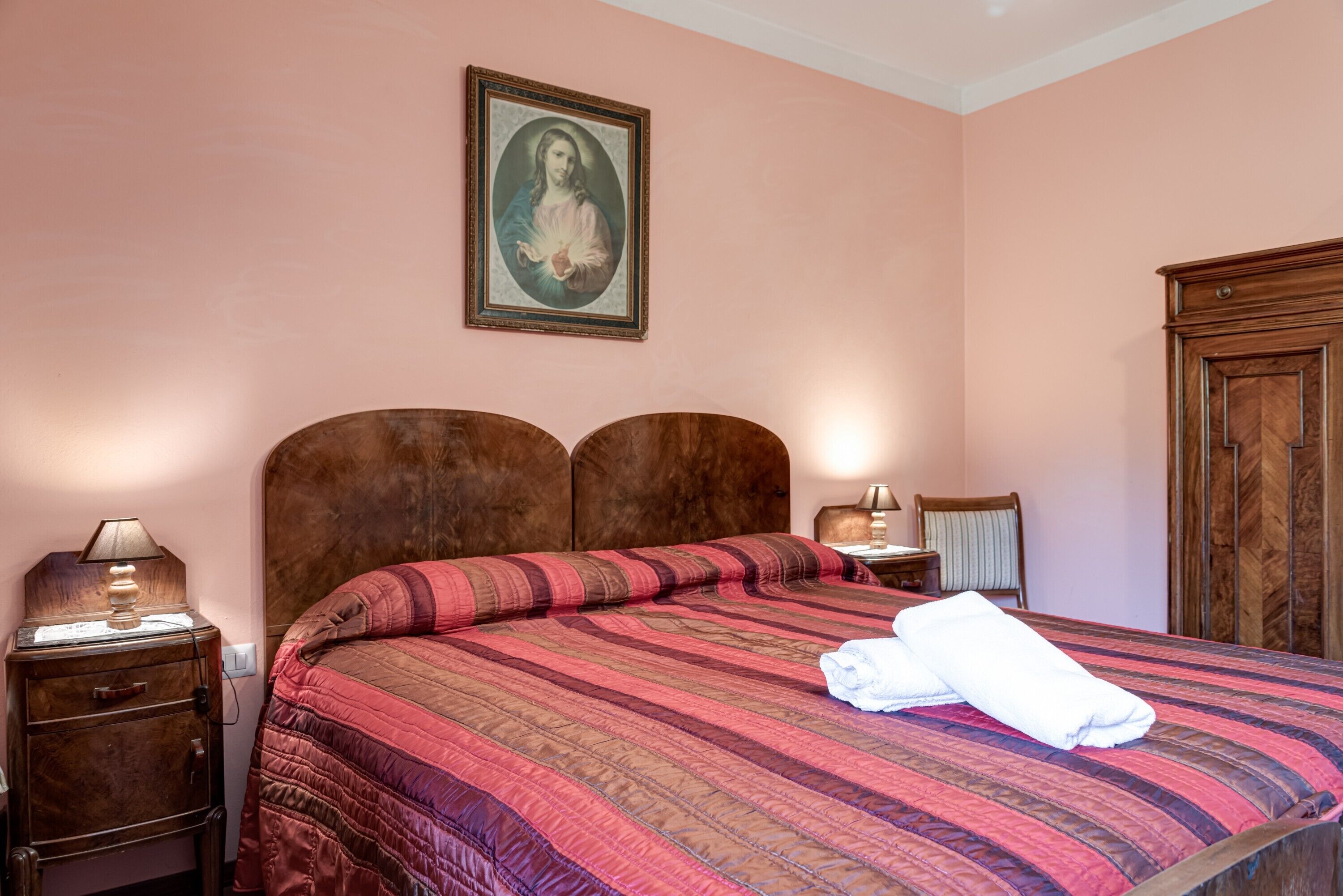 A bedroom with a bed, wooden headboard, nightstands, a lamp, a framed picture on the wall, and a wardrobe.