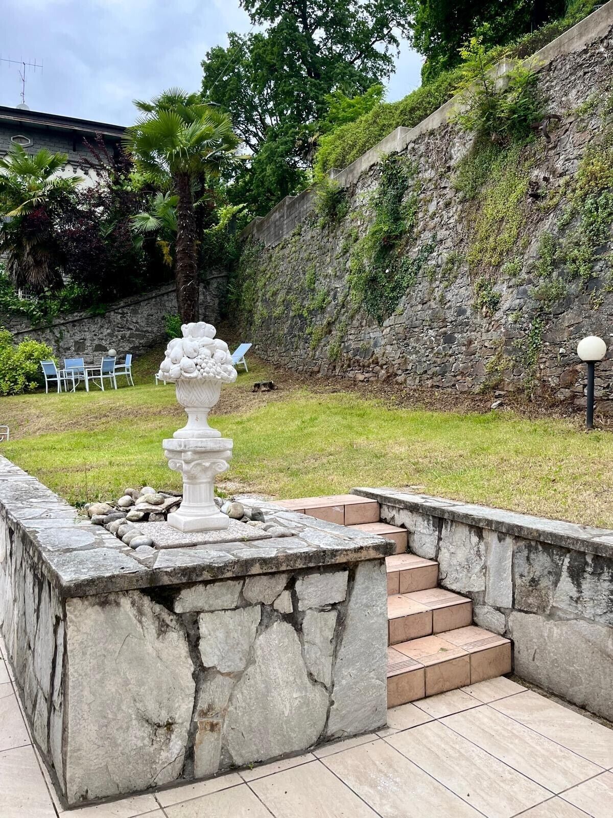 A stone fountain in a garden with steps leading up to a seating area.