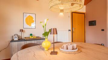 Un coin repas avec une table ronde en bois, un vase jaune orné de fleurs, une lampe et un plateau avec des tasses.