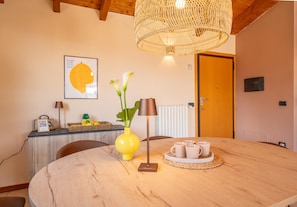A dining area with a round wooden table, a yellow vase with flowers, a lamp, and a tray with cups.
