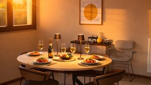 Un coin repas avec une table ronde, quatre chaises, une bouteille de vin, des verres et un tableau encadré au mur.