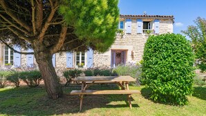 Un bâtiment en pierre avec une table de pique-nique en bois et un grand arbre au premier plan.
