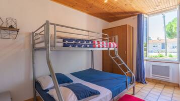 A bunk bed room with a wooden ceiling, a window with curtains, and a view of the outside.