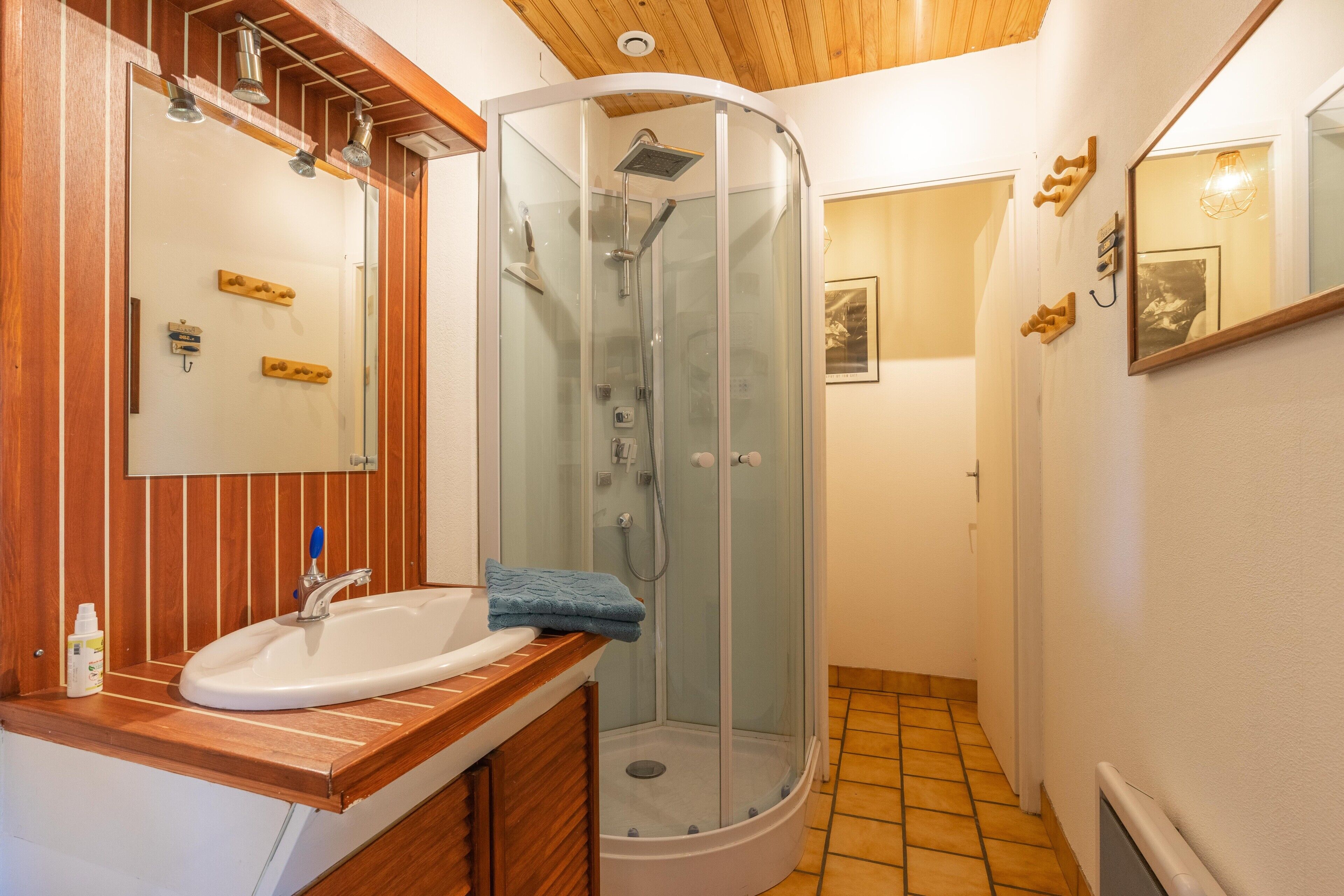 Une salle de bain dotée d’une douche à parois de verre, d’un meuble-lavabo en bois et d’un lavabo blanc.