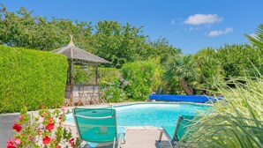 Une piscine entourée de chaises longues, d’un belvédère et d’une végétation luxuriante.