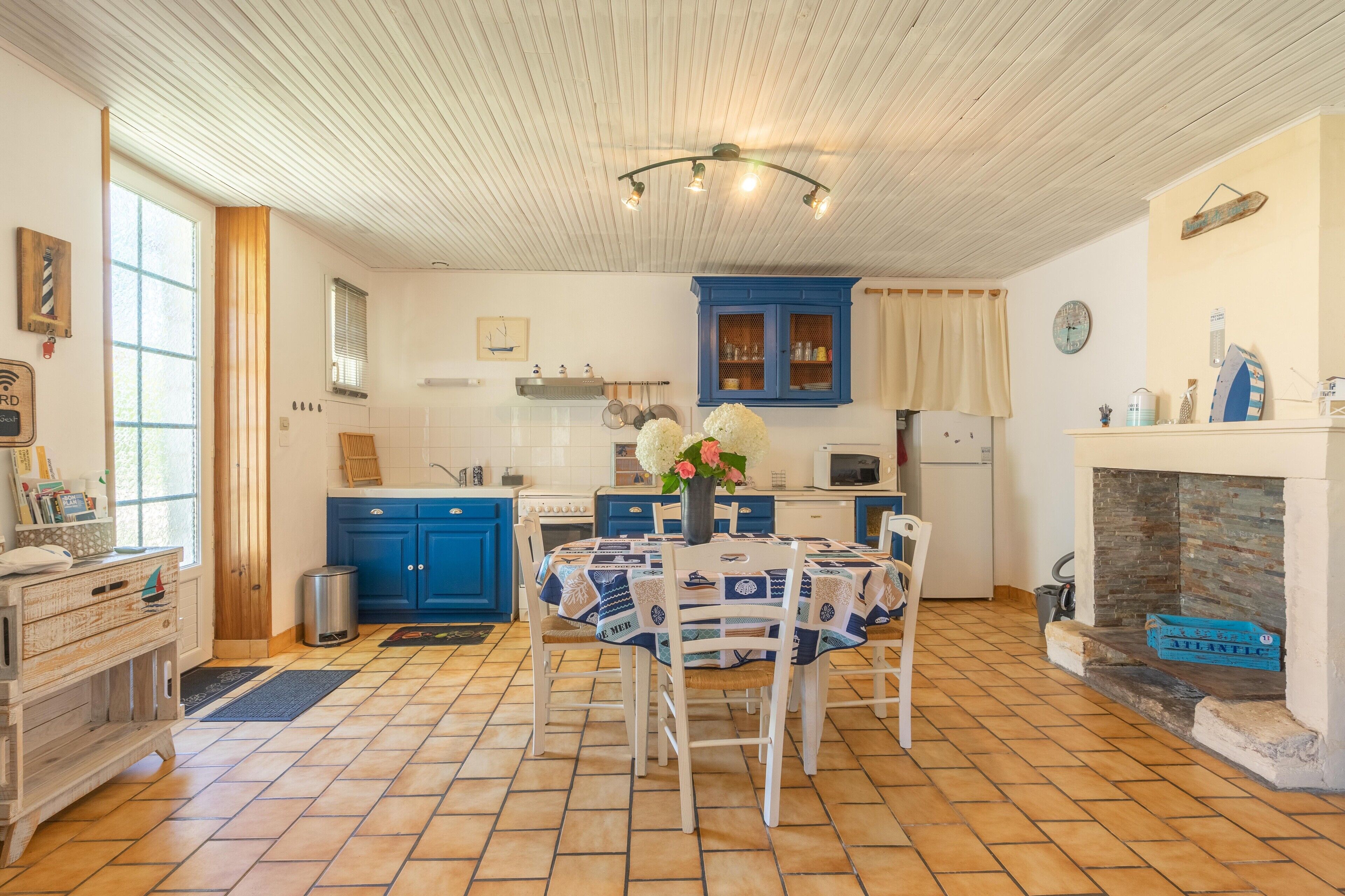 A kitchen with blue cabinets, a dining table with a patterned tablecloth, and a fireplace.