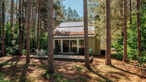 Une cabane entourée de grands arbres, dotée d’un porche couvert et d’un espace extérieur aménagé pour s’asseoir.