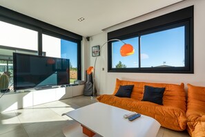 Una sala de estar moderna con un televisor de pantalla plana, un sofá, una mesa de centro y un ventanal con vistas al exterior.