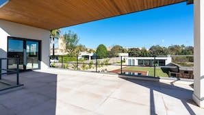 Een modern buitenpatio met houten overkapping, een glazen deur en uitzicht op een woonwijk met huizen en groen.