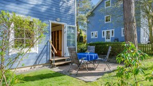 Una casa azul con una terraza de madera, una mesa con sillas y una puerta que da al interior.
