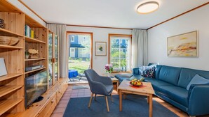 Una sala de estar acogedora con un sofá azul, una estantería de madera y un televisor.