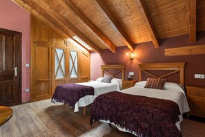 Una habitación con dos camas, vigas de madera en el techo, un armario de madera y una lámpara fijada a la pared.