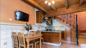 Eine Küche mit Holzschränken, einem Esstisch mit Stühlen, einem an der Wand montierten Fernseher und einer Treppe mit einer Zierrelung.