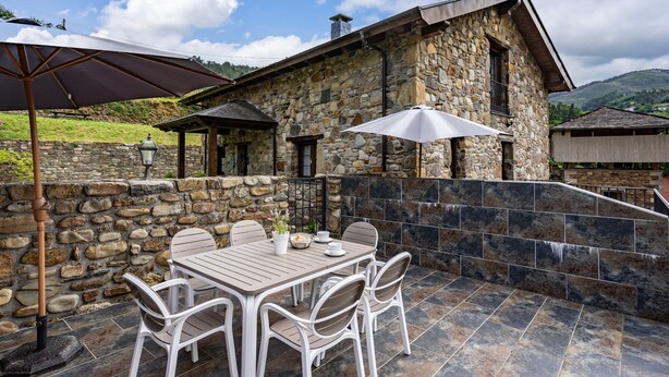 Ein Steinhaus mit einer Terrassenfläche, die einen Tisch, Stühle, eine Pergola und eine Steinmauer zeigt.