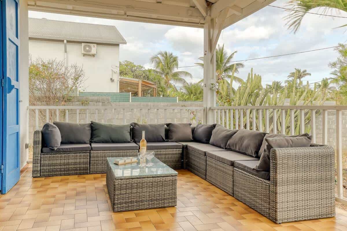 A covered outdoor seating area with a wicker sofa and a glass coffee table.