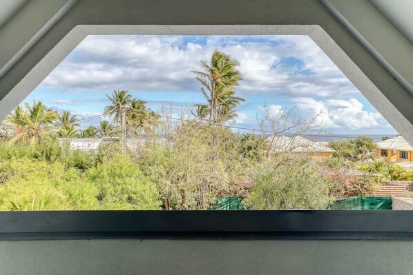 Vista a través de una ventana con cielo despejado, palmeras y un edificio al fondo.