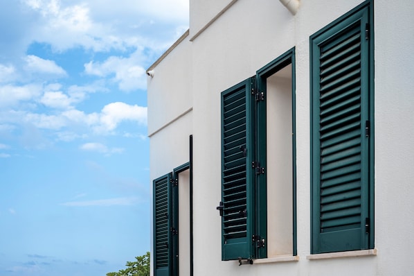 A building with three windows, each with green shutters, and a clear sky in the background.