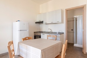 A compact kitchen with a refrigerator, stove, oven, and sink. There is a table with chairs and a door leading to a shower area.