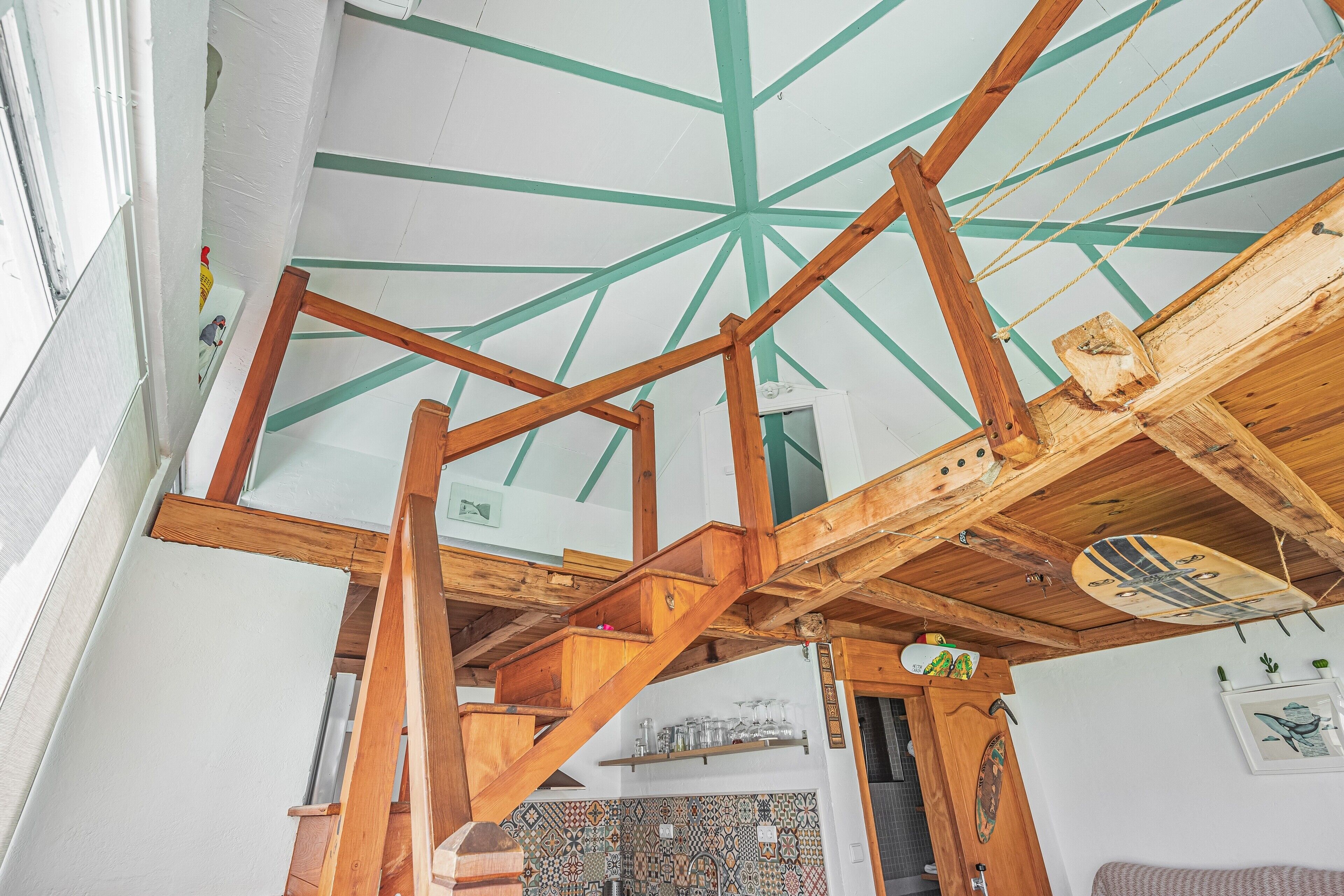 A wooden staircase with a geometric ceiling design, a tiled wall, and a surfboard decoration.