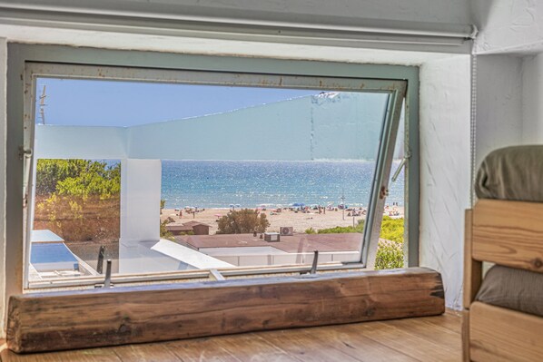 A view through a window of a beachside property with a wooden floor, a white wall, and a clear blue sky.