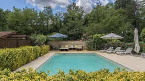 A swimming pool with lounge chairs and umbrellas, surrounded by greenery and a stone wall. - Holiday Home 'Cascina Oddone Prati Winery' with Shared Pool, Wi-Fi and Air Conditioning (Strevi)