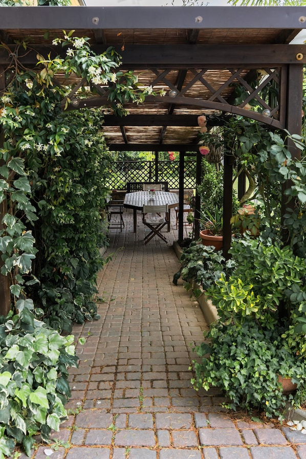 Un patio couvert avec un sol en briques, une pergola en bois et une table entourée de chaises.