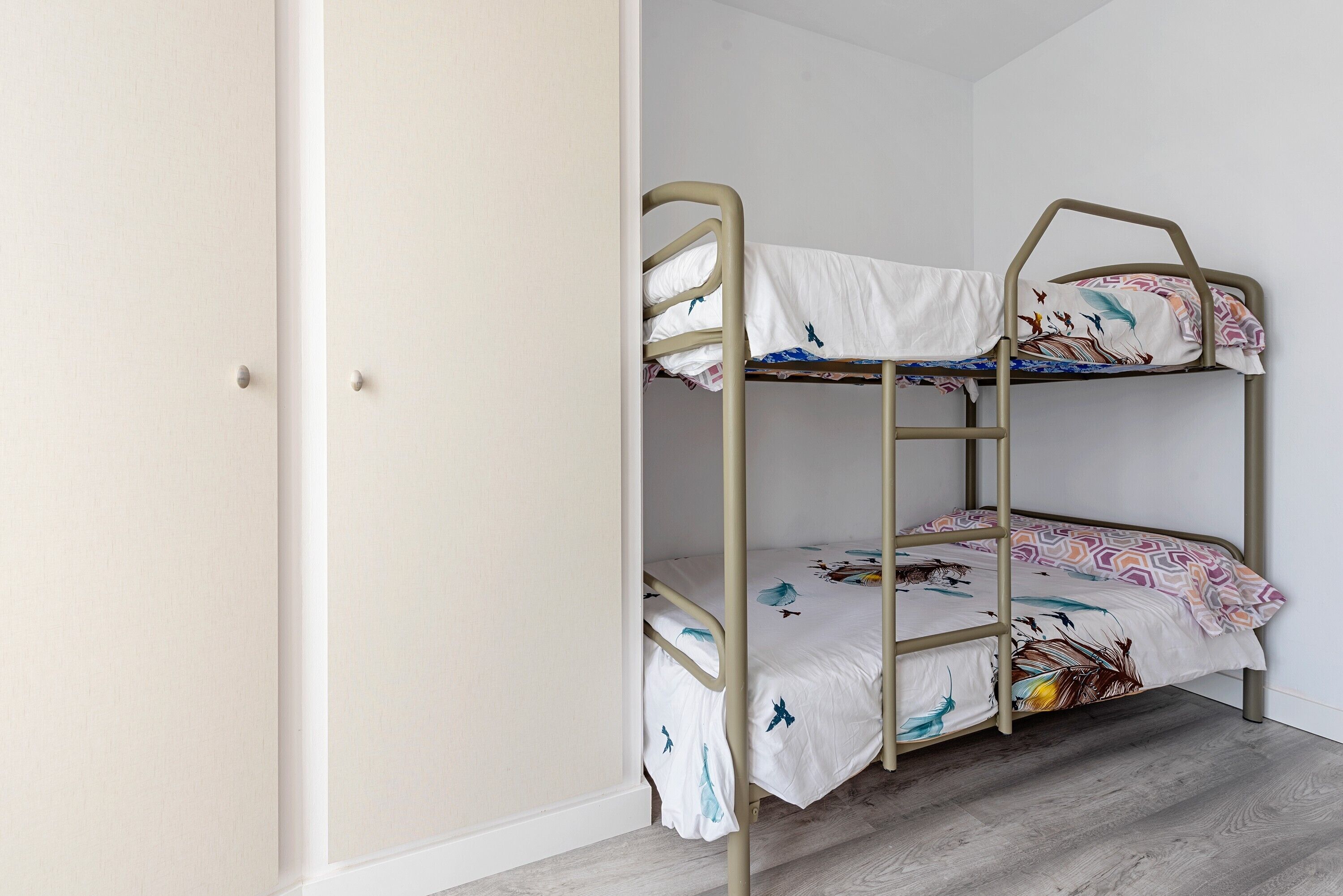 A bunk bed with a white mattress and patterned bedding, a wooden floor, and a white door.