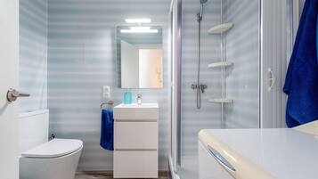 Un baño con inodoro, lavamanos con espejo, ducha y una toalla azul.