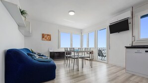 Un apartament modern amb un sofà blau, taula de menjador, cadirees i zona de cuina.