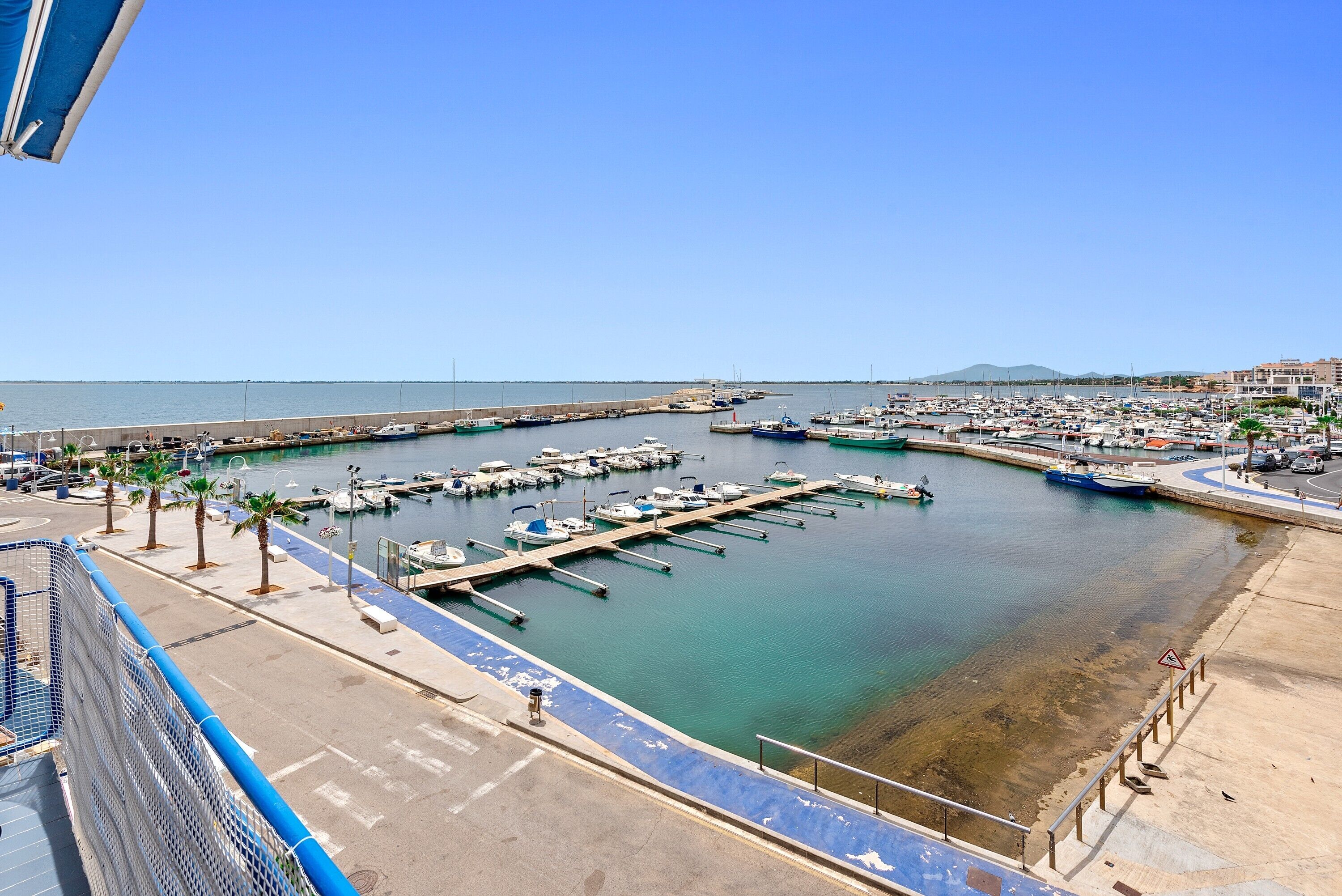 Un port de plaisance avec des bateaux amarrés, un ciel dégagé et une montagne qui se profile à l’horizon.
