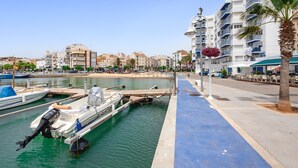 Un port esportiu amb embarcacions amarrades, un camí pavimentat blau per a vianants i un edifici amb balcons.
