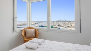 Habitació amb un llit, una cadira i vista a un port esportiu ple de vaixells.