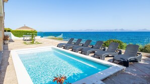 A swimming pool with lounge chairs, a thatched roof structure, and a view of the sea and mountains. - Villa 'Ca'n Torrens' with Sea Views, Wi-Fi and Air Conditioning (Alcúdia)